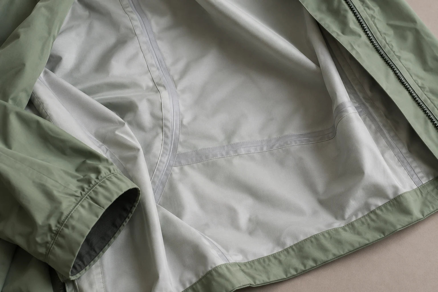 Interior de una chaqueta impermeable verde con cintas de sellado visibles sobre las costuras